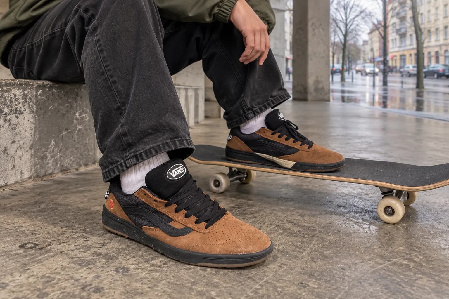 Скейтер в коричнево-черных кроссовках Vans поставил ногу на скейтборд.